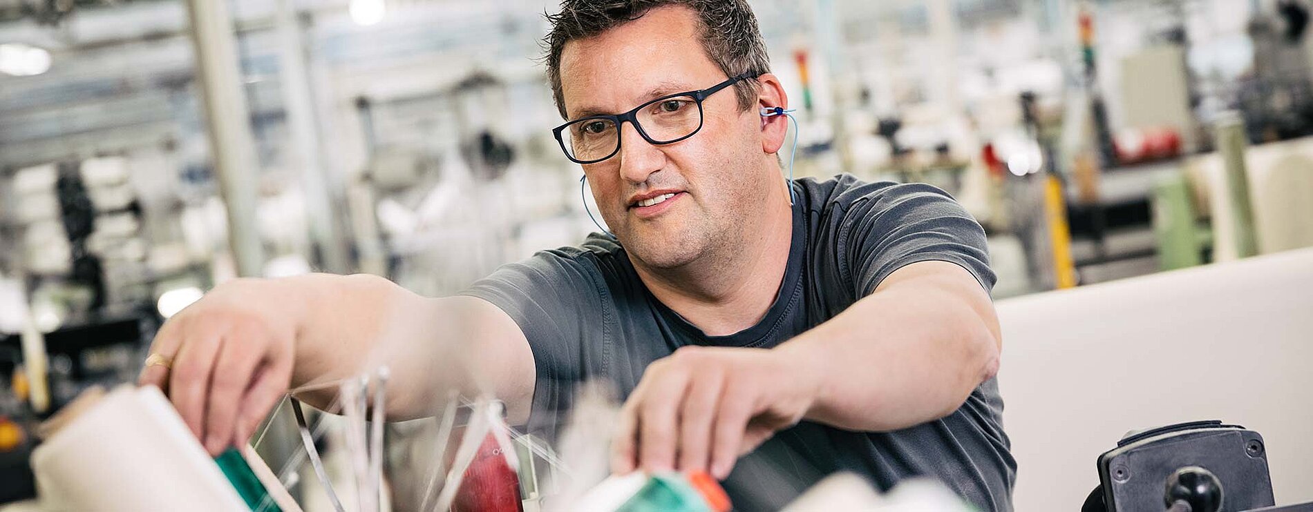 Mitarbeiter mit Brille bei der Arbeit an einer Textilmaschine in der Produktion von Velener