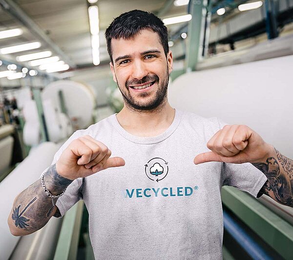 Mitarbeiter trägt ein T-Shirt mit dem WECYCLED®-Logo und zeigt es mit beiden Händen