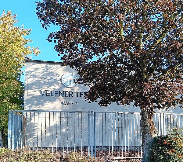 Gebäude von Velener Textil mit Firmenlogo, umgeben von Bäumen